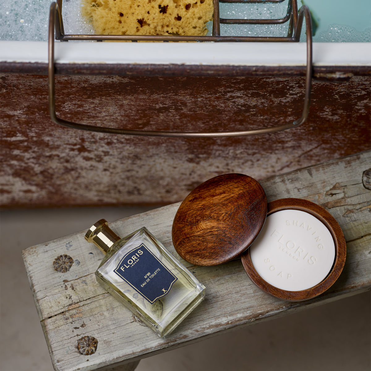 A bottle of Floris London perfume and a No. 89 Aftershave Balm rest on a rustic bench by the bathtub.