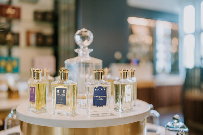 A display of Floris London fragrances showcased on a round marble stand, featuring elegant glass bottles with gold caps. Prominent labels include 