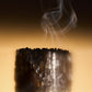 Celest - Eau de Parfum by Floris London UK evokes a smoking, charred candle stump set against a warm, golden backdrop.