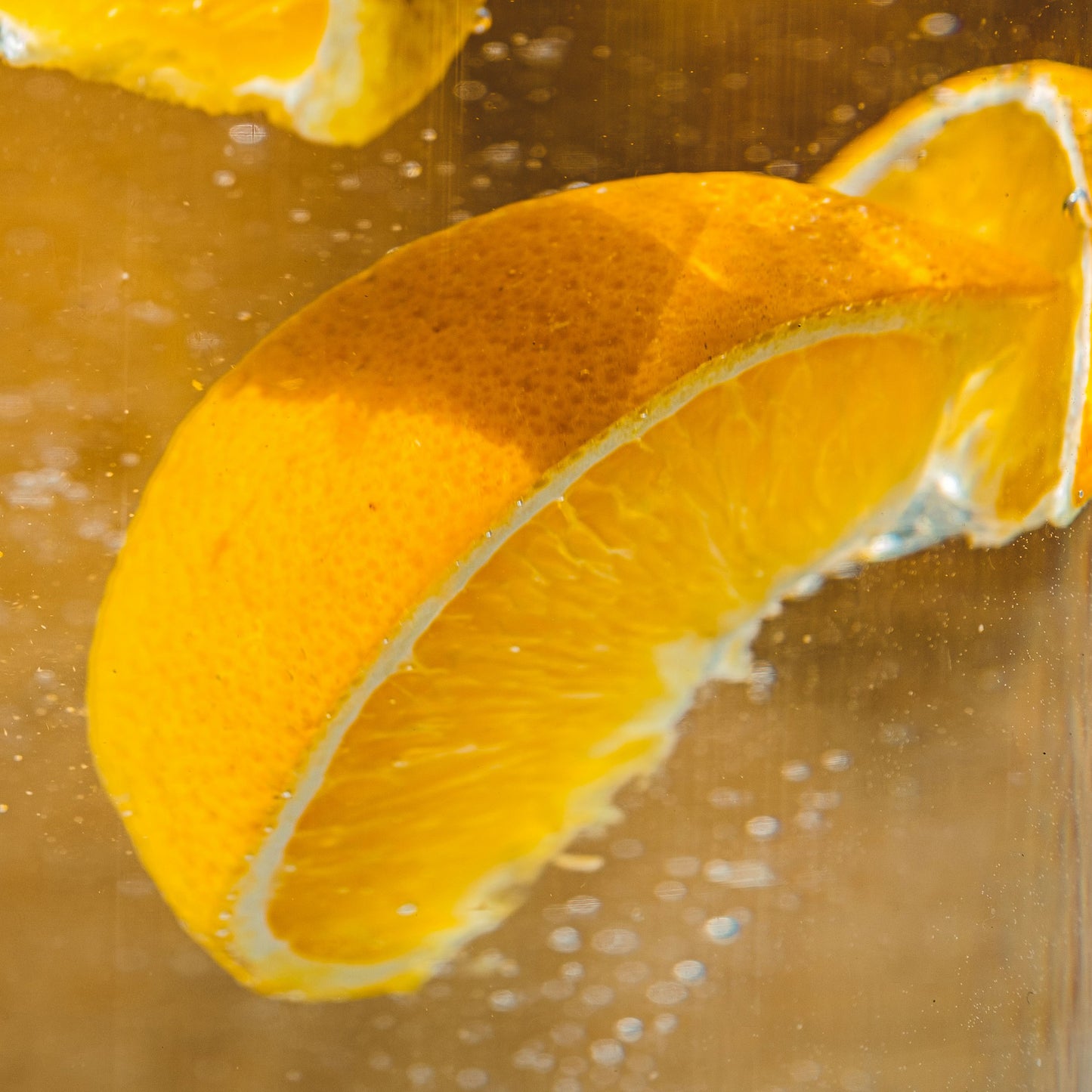 A close-up of an orange slice in sparkling water against a golden background, evoking the freshness of Floris London Cefiro - Eau de Toilette.